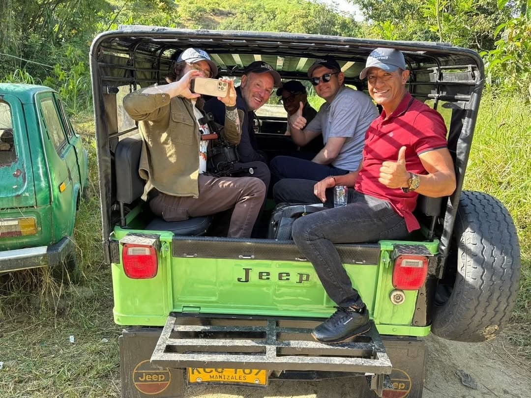 The trip group riding in the back of an open green Jeep on a farm track