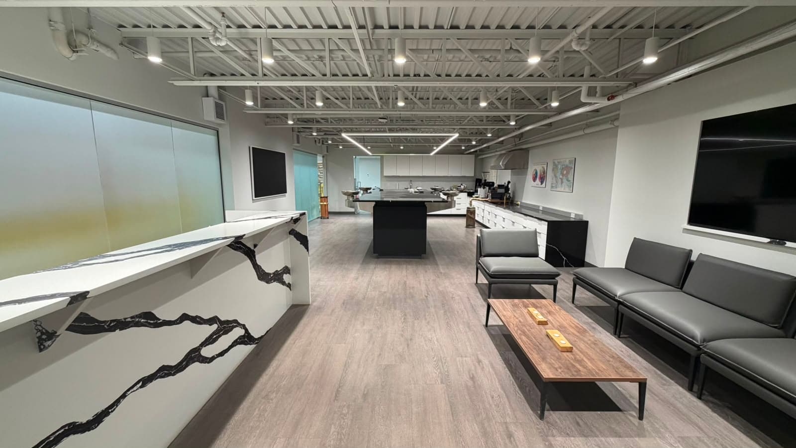 A wide view down the cupping room, a marble counter along the left, a seating area on the right, and the black cupping table in the middle distance.