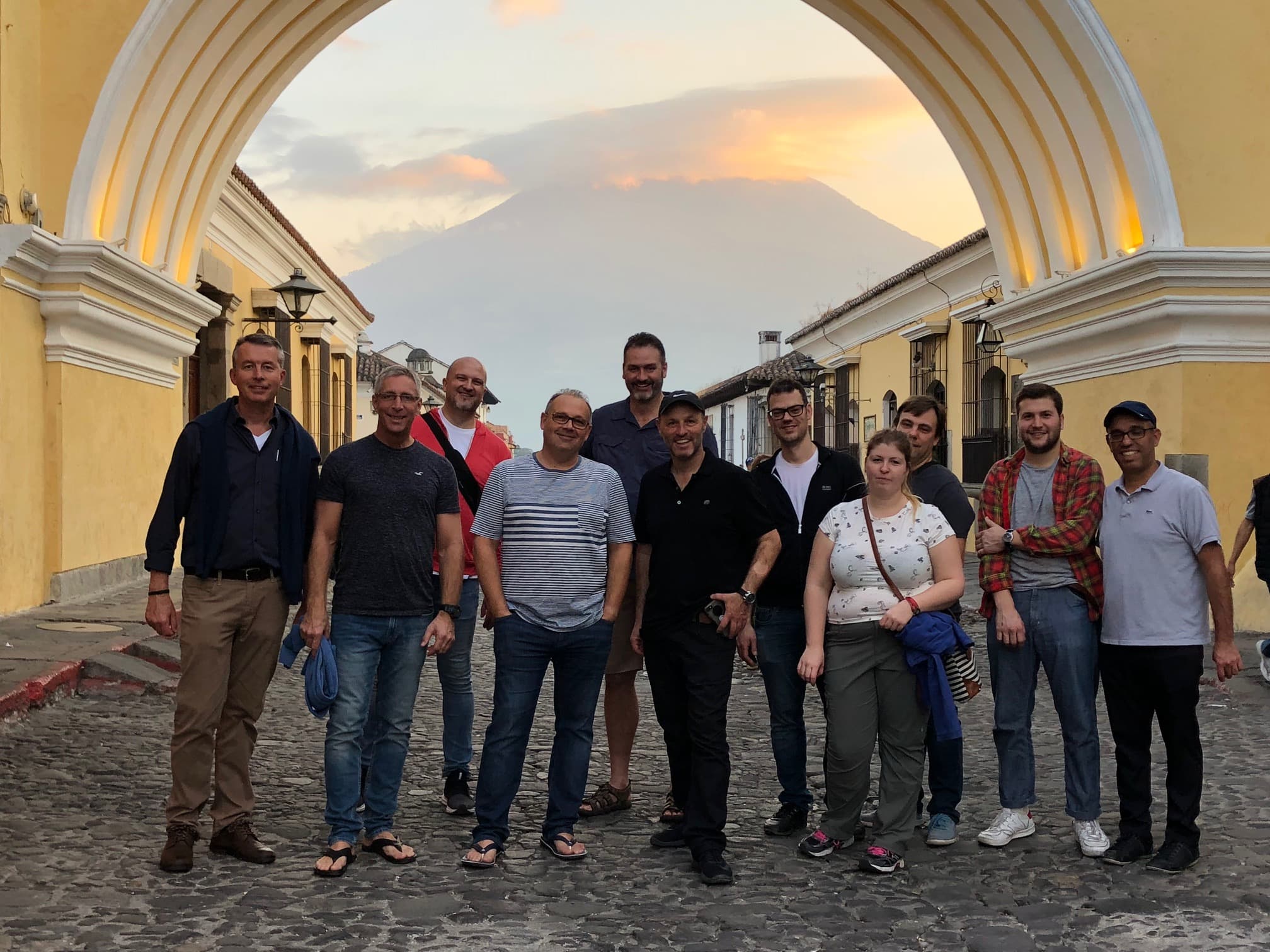 Customer trip group under the arch in Antigua with a volcano behind