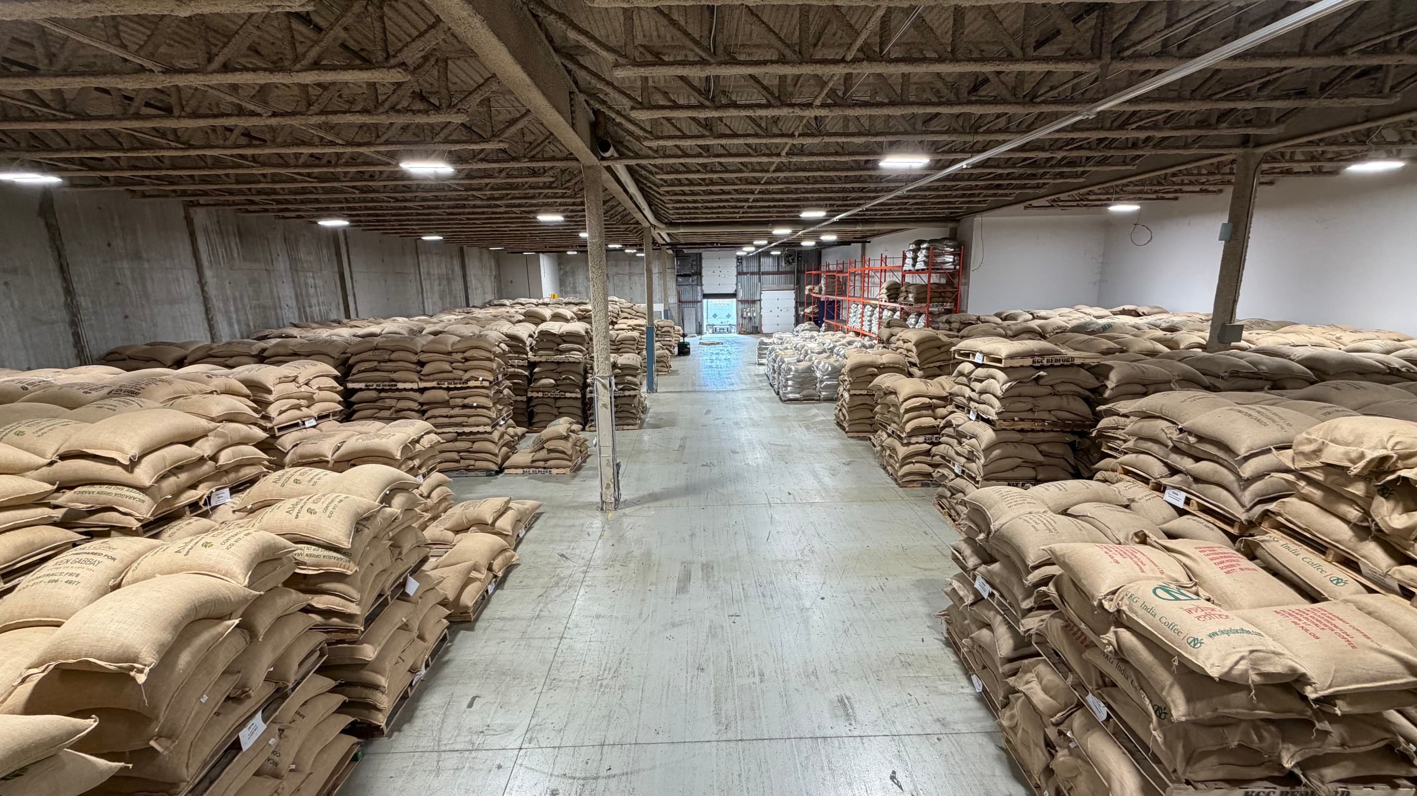 The center aisle of the Montreal warehouse leading to the loading dock, pallets of jute coffee bags stacked on both sides.