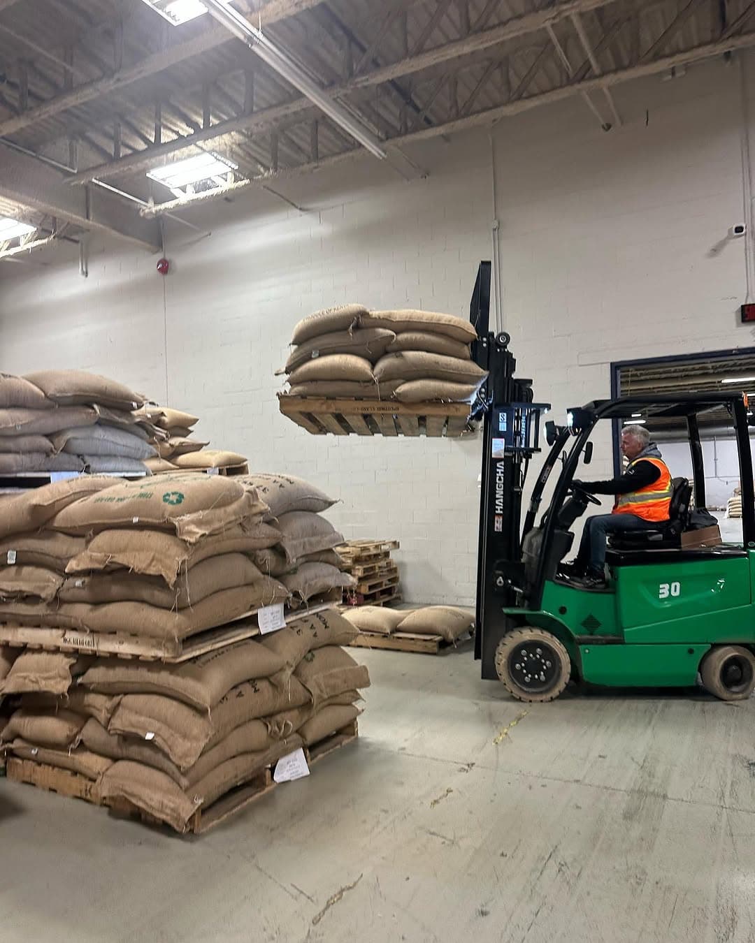 A warehouse operator on a forklift lifting a pallet of jute coffee bags.